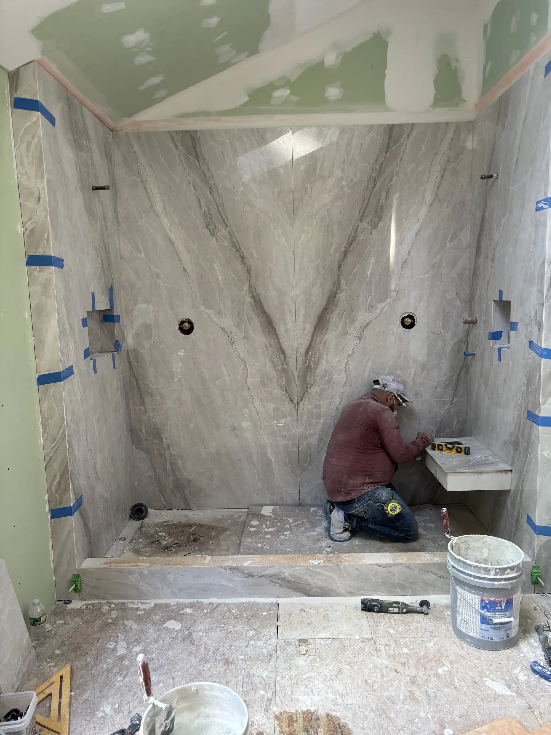 A Benchmark tile setter finishing the bench and floor tile in a marble-look shower