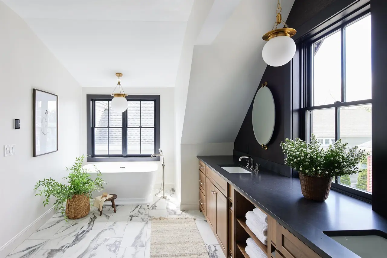Bathroom design inspiration: a primary bath with a freestanding soaking tub under the window, a marble tile floor, and a wood double vanity with a honed black countertop