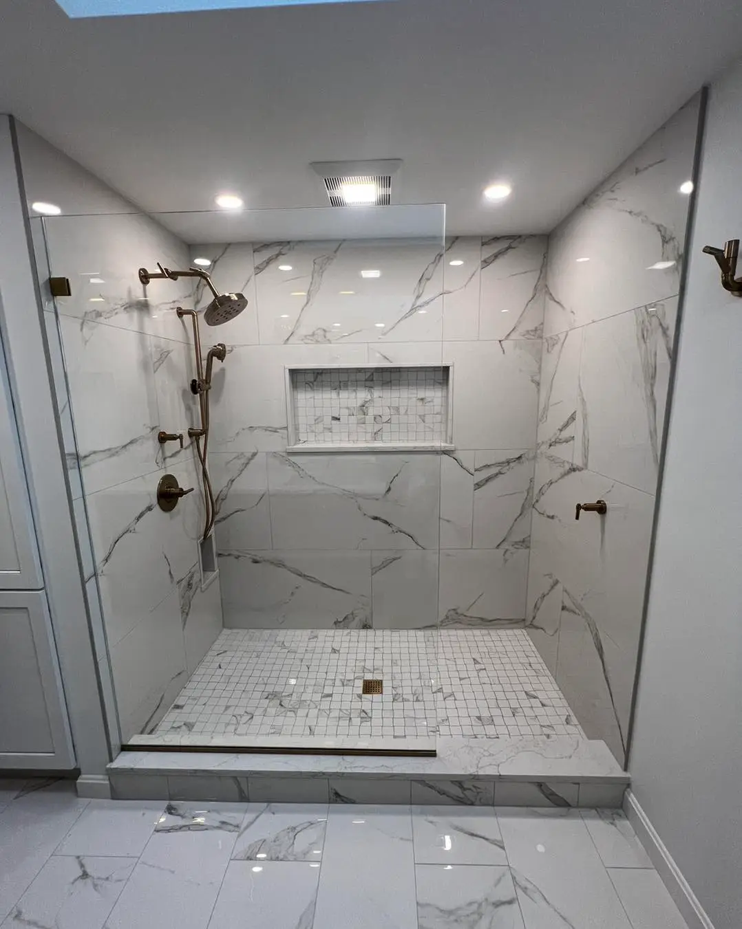 Bathroom design inspiration: a walk-in shower in white marble-look porcelain tile with brushed brass fixtures and a marble mosaic shower floor
