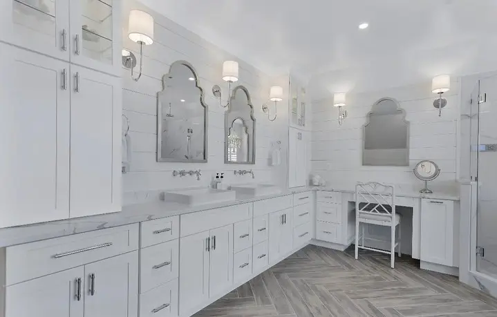 White bathroom with a double vanity, arched mirrors, shiplap walls, and a herringbone tile floor, remodeled by Benchmark on the New Hampshire Seacoast