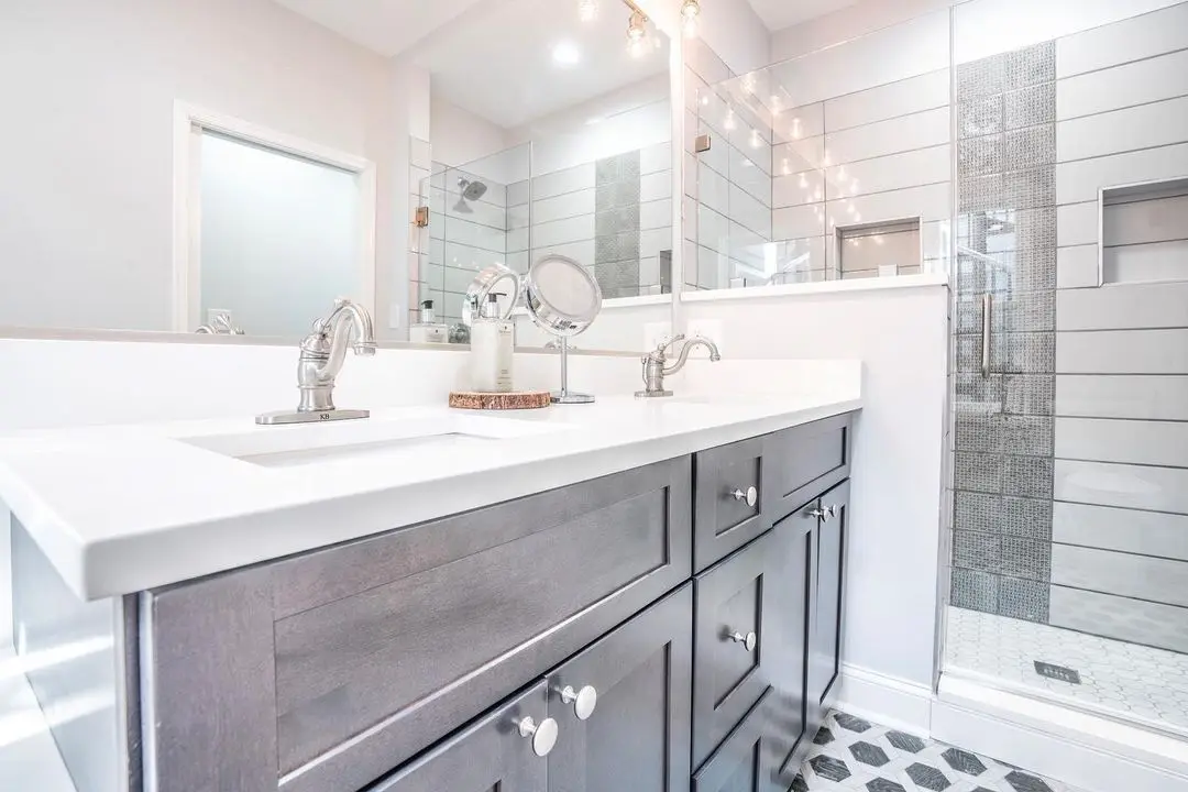 Bathroom with a grey vanity, white quartz top, and a tiled glass shower, remodeled by Benchmark on the New Hampshire Seacoast
