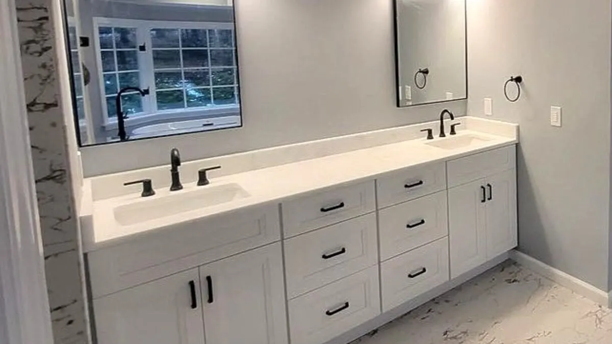A finished bathroom with a white double vanity, large mirrors, and marble-look tile, remodeled by Benchmark on the New Hampshire Seacoast