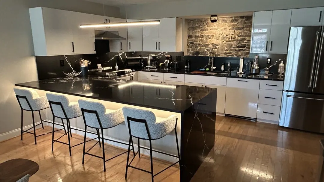 A remodeled kitchen with a dark stone peninsula, seating for four, and white cabinets along two walls