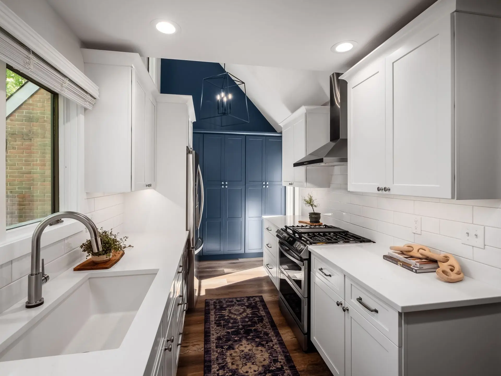 White and navy galley kitchen with a navy accent wall, remodeled by Benchmark on the New Hampshire Seacoast