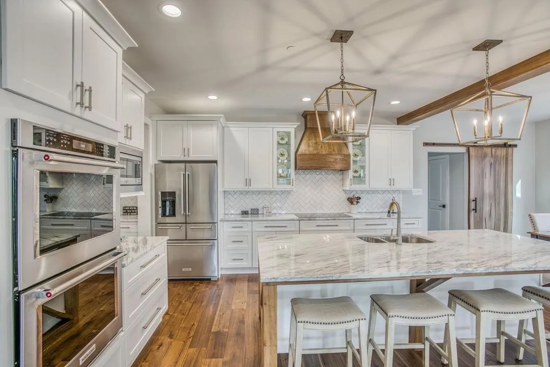 White kitchen with a wood range hood, lantern pendants, and a marble waterfall island, remodeled by Benchmark on the New Hampshire Seacoast