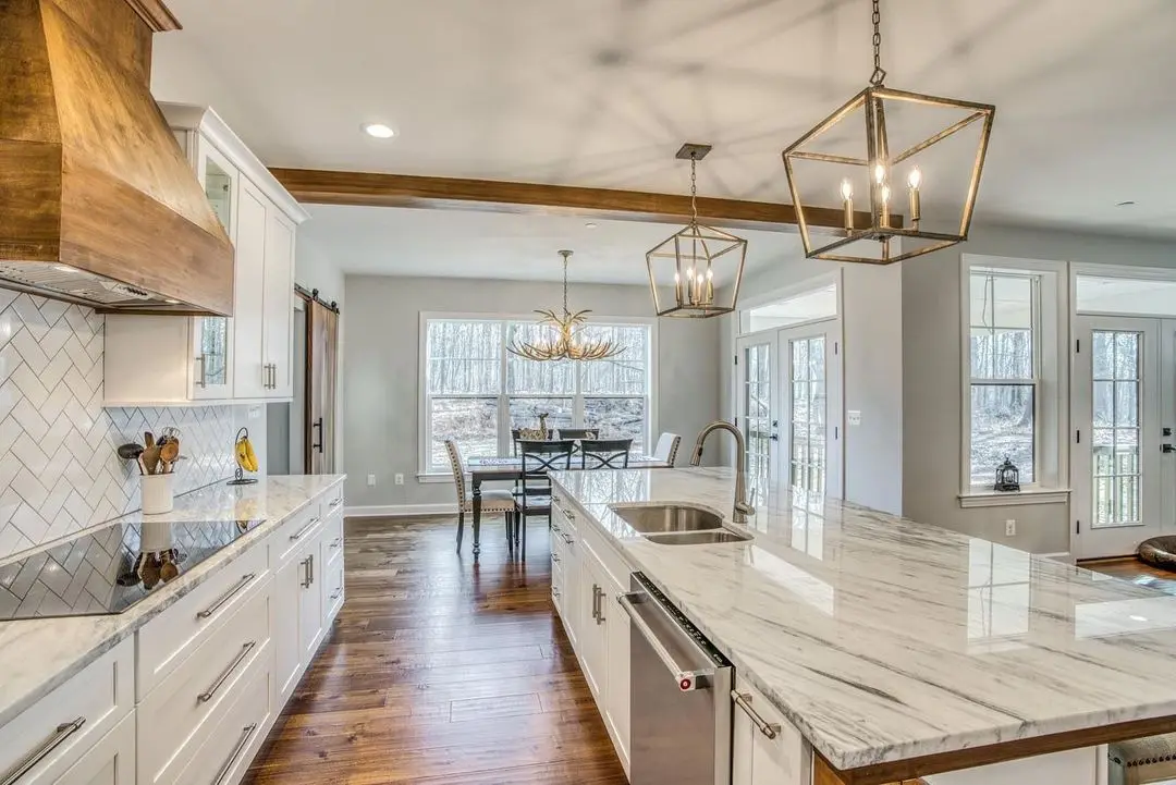 White kitchen with a wood range hood, marble island, and a breakfast nook under wood beams, remodeled by Benchmark on the New Hampshire Seacoast
