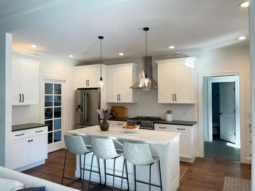 White shaker kitchen with a marble-top island and glass pendant lights, remodeled by Benchmark on the New Hampshire Seacoast