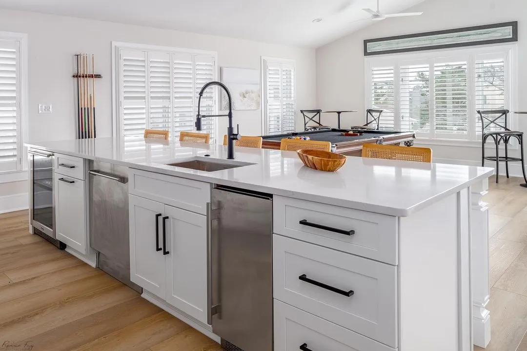 Open-concept white kitchen with a long quartz island and black fixtures, remodeled by Benchmark on the New Hampshire Seacoast