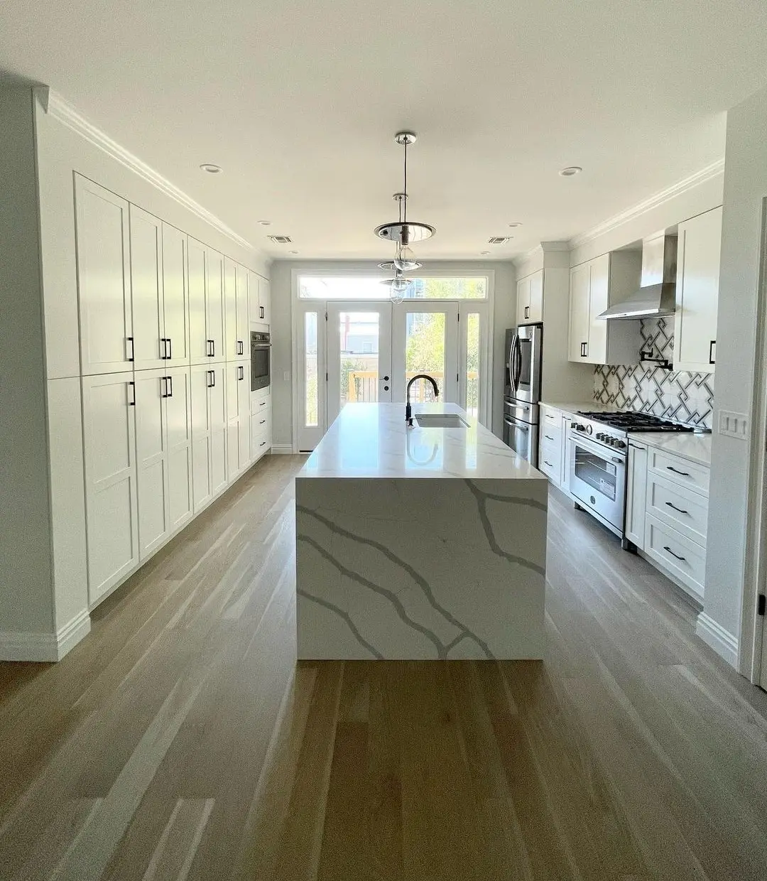 Long white kitchen with a quartz waterfall island, professional range, and French doors, remodeled by Benchmark on the New Hampshire Seacoast