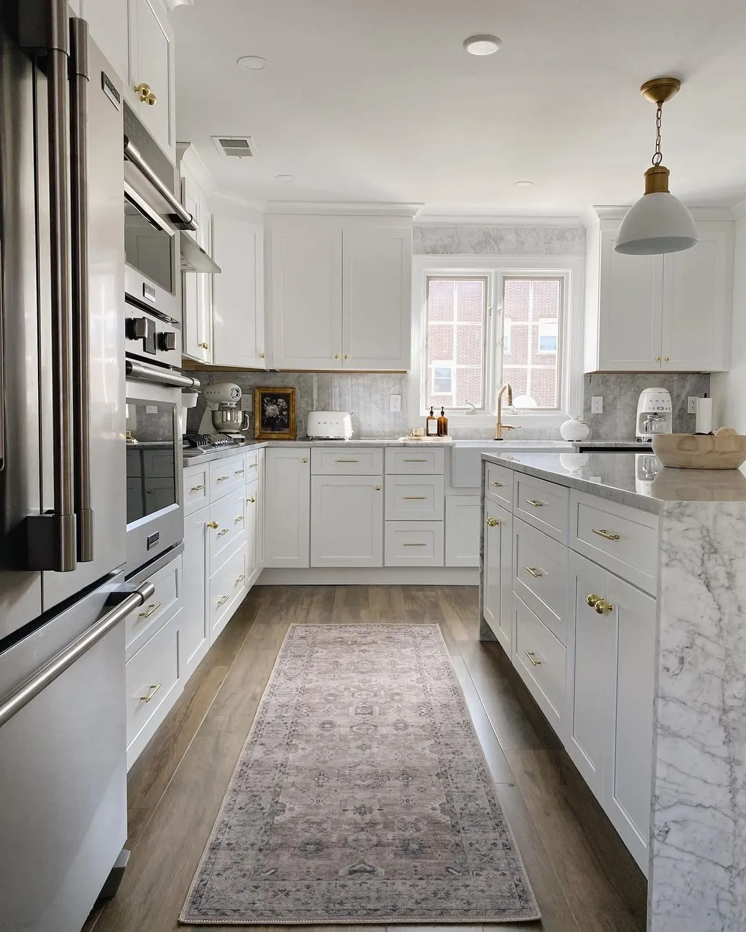White kitchen with marble countertops, gold hardware, and a farmhouse sink, remodeled by Benchmark on the New Hampshire Seacoast