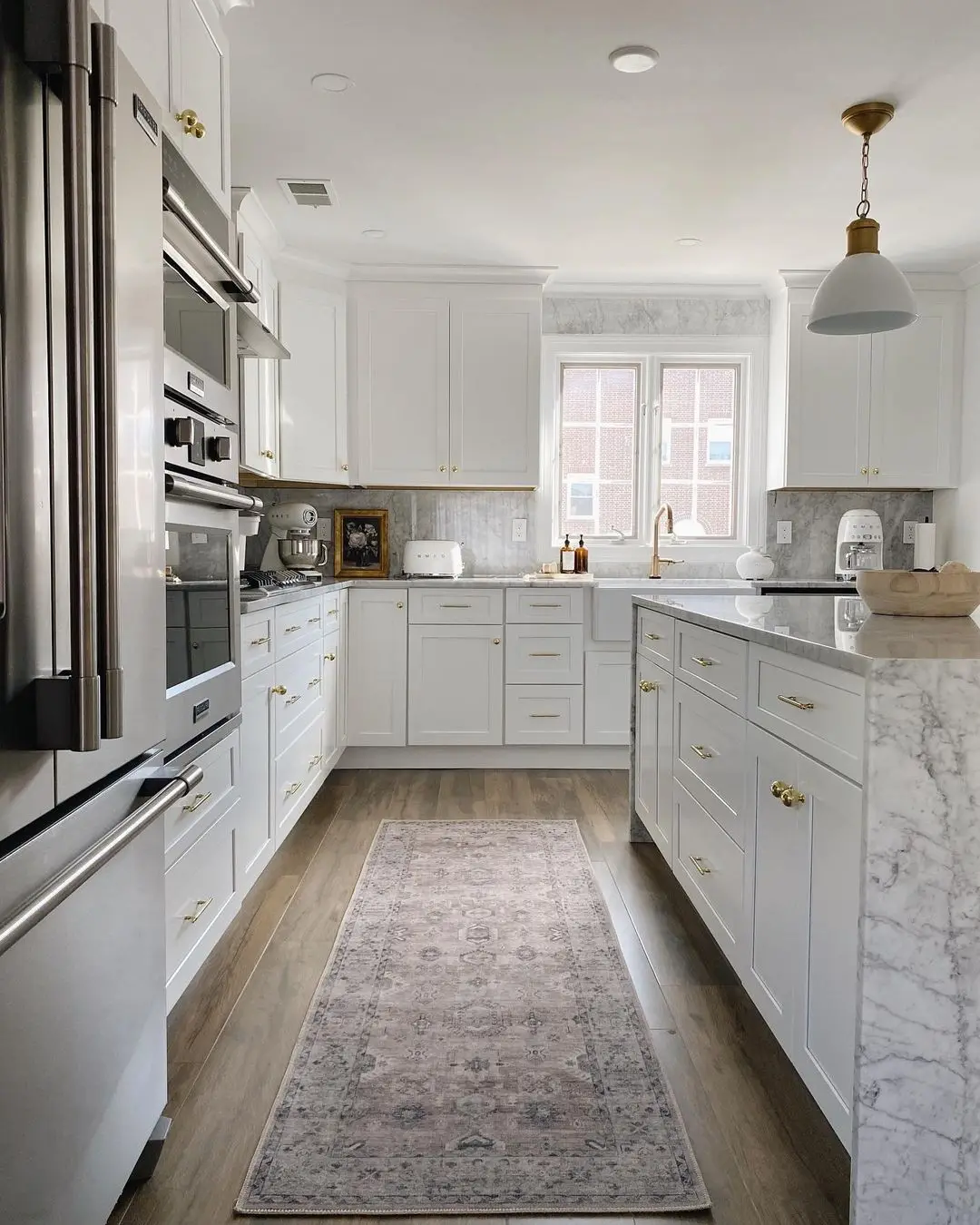 White kitchen with marble countertops, gold hardware, and a farmhouse sink, remodeled by Benchmark on the New Hampshire Seacoast