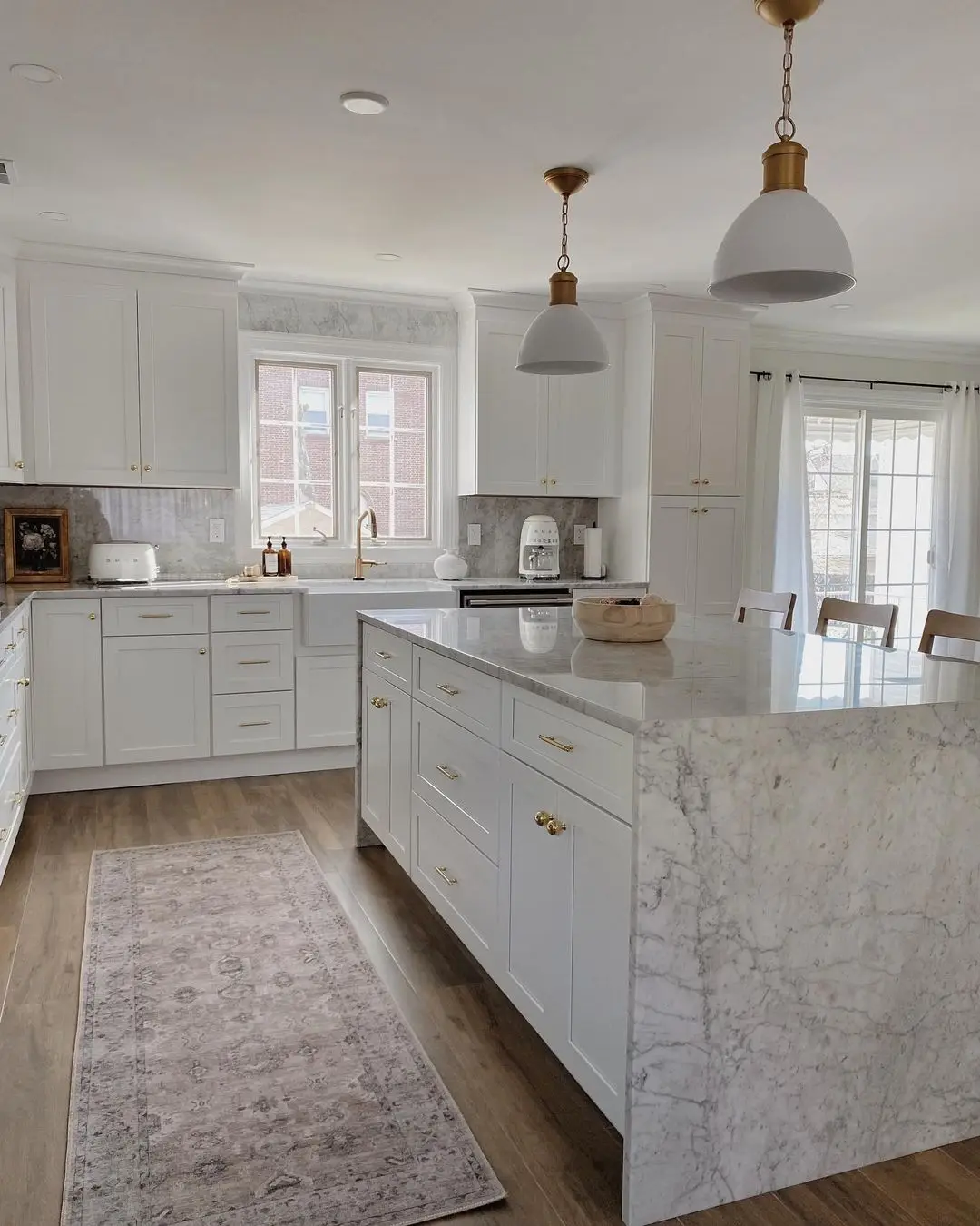 White kitchen with a marble waterfall island and brass dome pendants, remodeled by Benchmark on the New Hampshire Seacoast