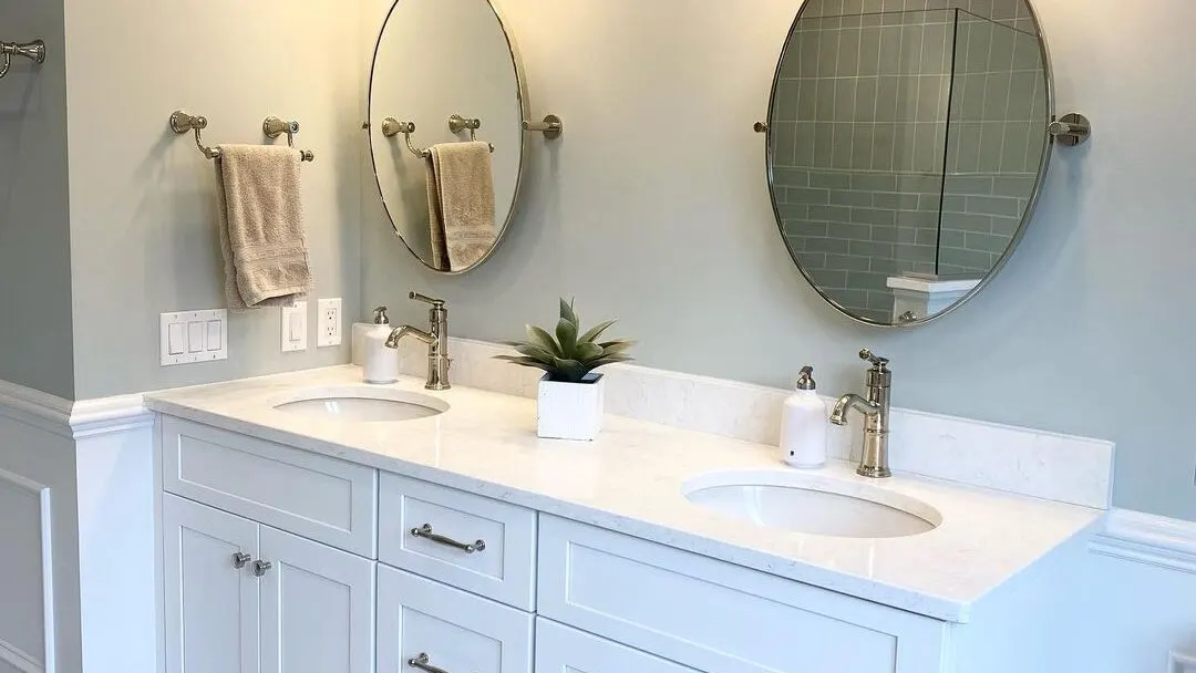 A renovated bathroom with sage-green walls, a white double vanity, and classic fixtures in an older Seacoast New Hampshire home by Benchmark