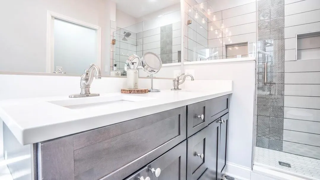 A compact bathroom with a grey vanity, white quartz, and a walk-in glass shower, remodeled by Benchmark on the New Hampshire Seacoast