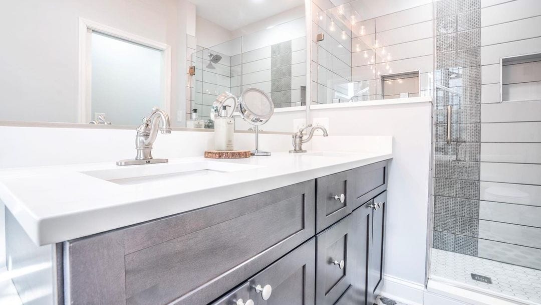 A remodeled bathroom with a double vanity, large mirror, and a tiled walk-in glass shower