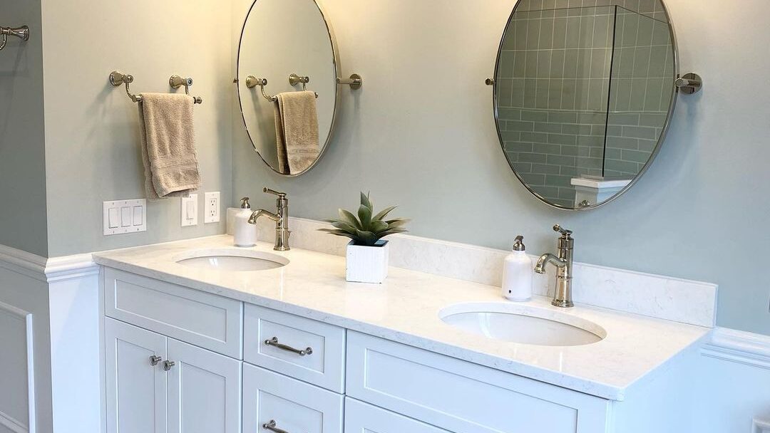 A renovated bathroom with sage-green walls, a white double vanity, and classic fixtures in an older Seacoast New Hampshire home by Benchmark